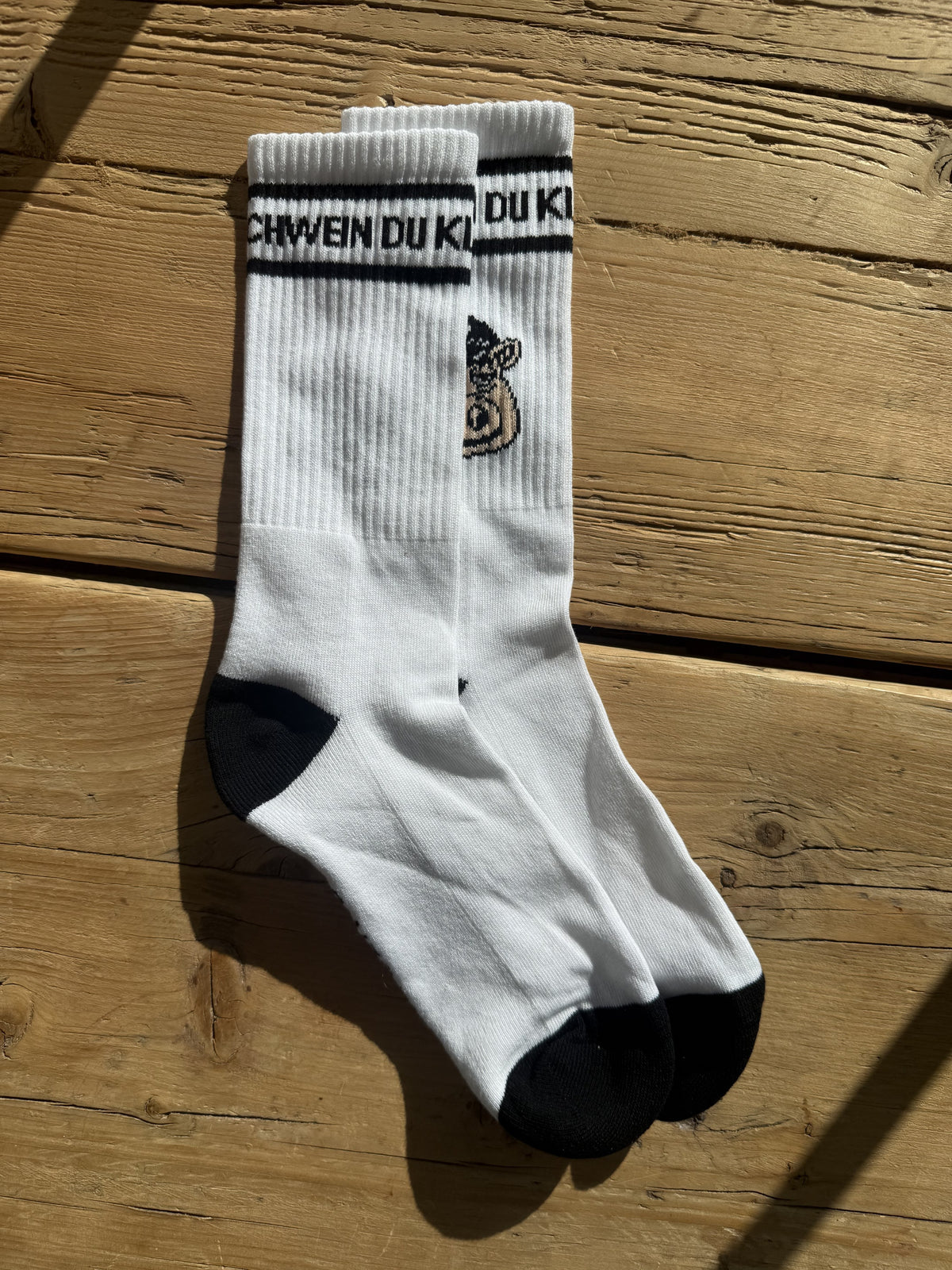 Socken gegen Faschos: das Paar auf Holzdielen, Bündchen „DU KLEINES NAZI SCHWEIN“ und Nazischwein