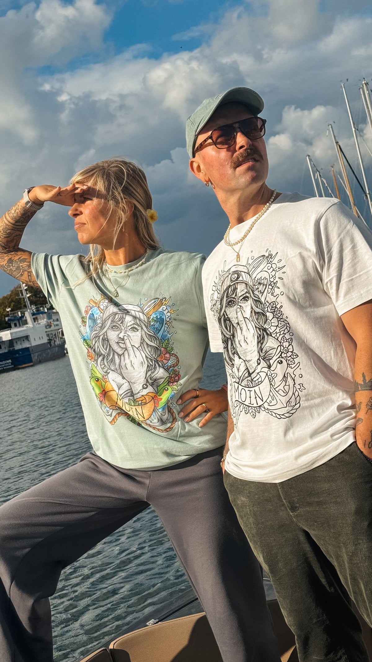 Zwei Models am Wasser; das weiße Shirt zeigt eine Kapitänin mit erhobenem Mittelfinger und MOIN.